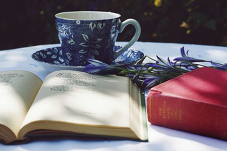 An open book in front of a teacup. 