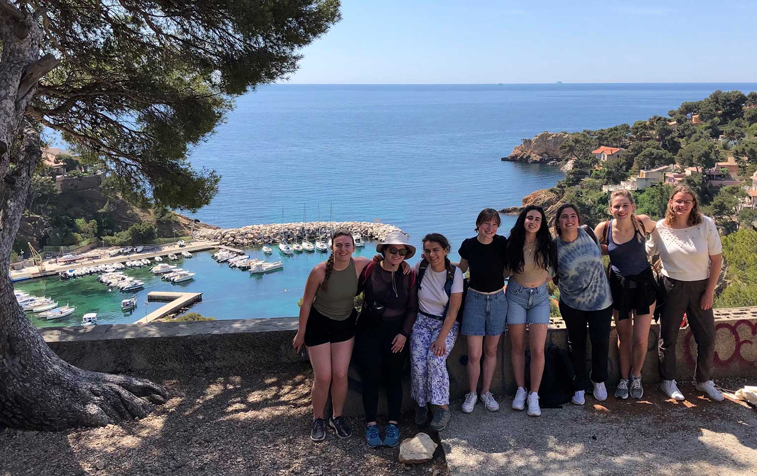 A group of students pose near a cliffside with the ocean in the background.