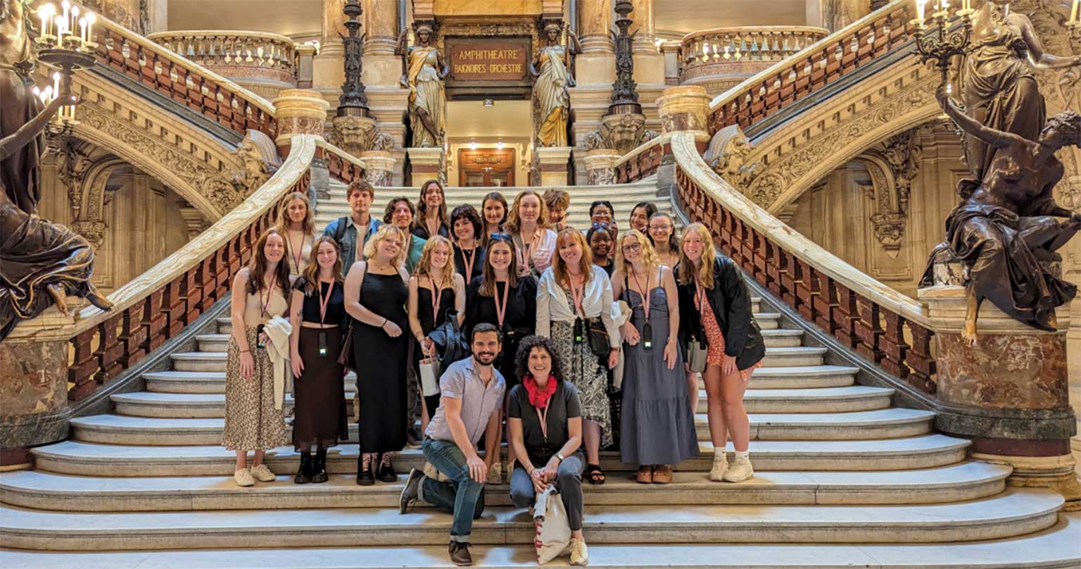 A group of students pose together on the steps of an ornate, winding staircase.