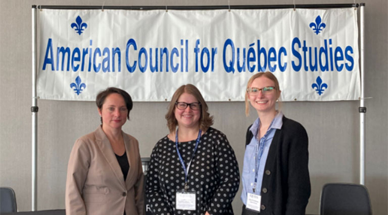 Three people pose in front of a banner that says "American Council for Québec Studies."