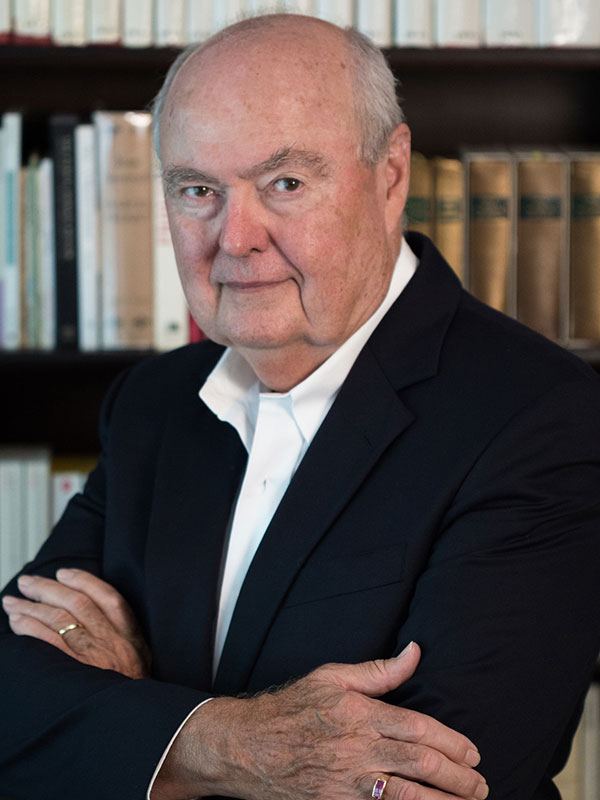 A headshot of William Carter, who poses against a bookshelf with his arms crossed over his chest.
