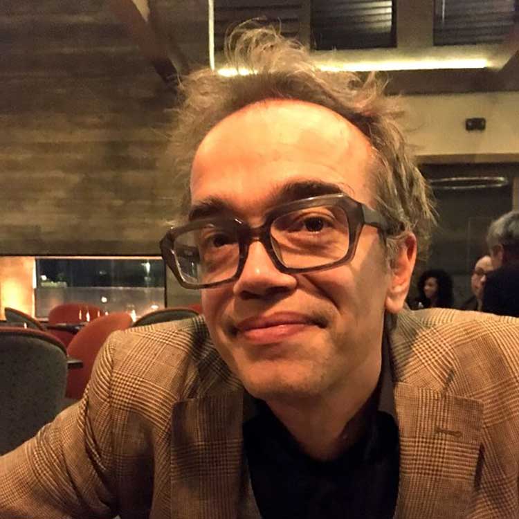 A headshot of Bjornstad Hall, who wears a brown shirt and poses with one hand on his chin.